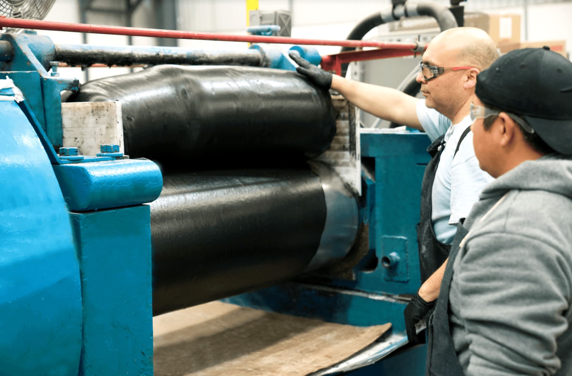 A steel mixer with rubber being processed while two men supervise the operation