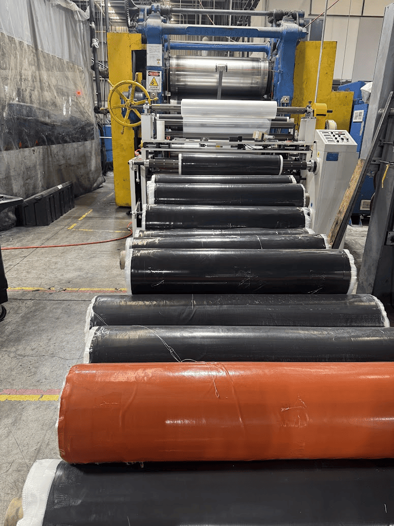 Several rolls of laminated rubber in front of a calendering machine