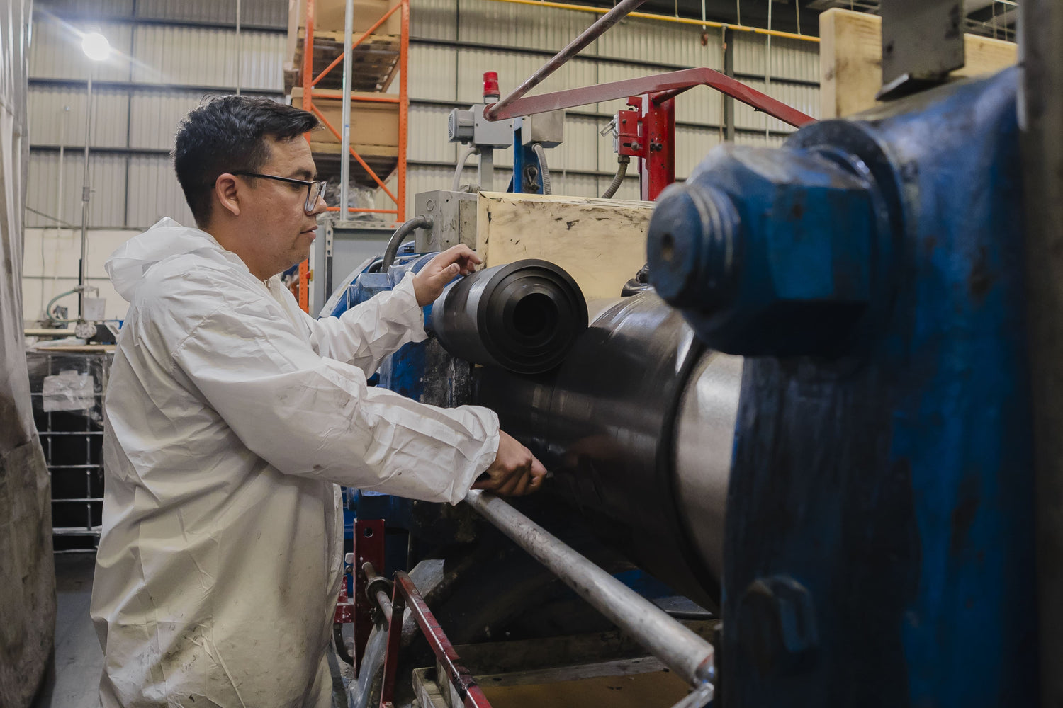 A steel mixer with rubber being processed while a man cuts the rubber